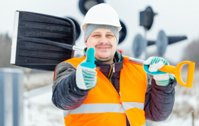 Worker with snow shovel near signal beacons in snowy day